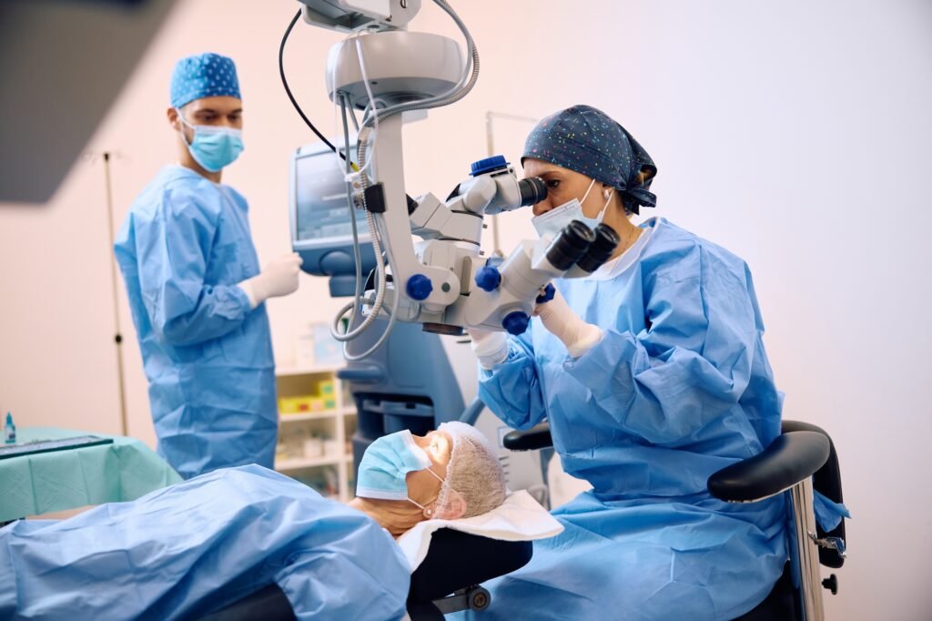 Female ophthalmologist looking through microscope during eye surgery of a patient.