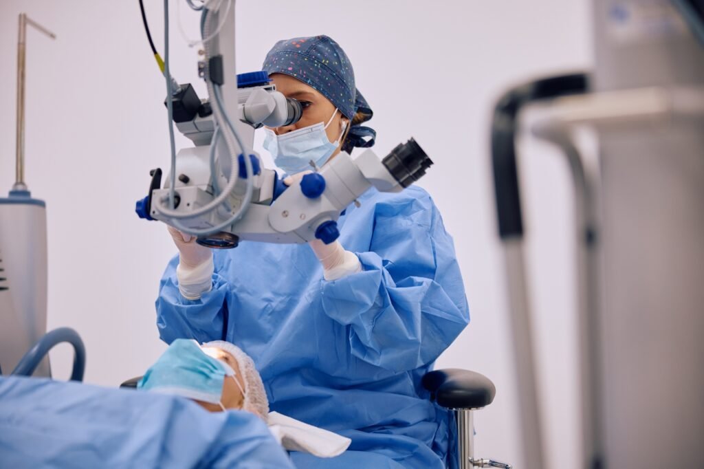 Female ophthalmologist performing eye surgery while using microscope in operating room.